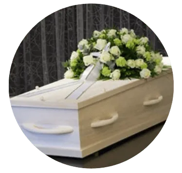 Cercueil en bois clair orné d'une composition florale de roses blanches et ruban de condoléances