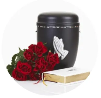 Urne cinéraire ornée de mains en prière posée à côté d'un bouquet de roses rouges et d'une bible